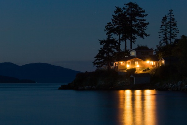 A home on the lake with all of the lights on, powered by whole home back up Generac generator by Generator Supercenter.