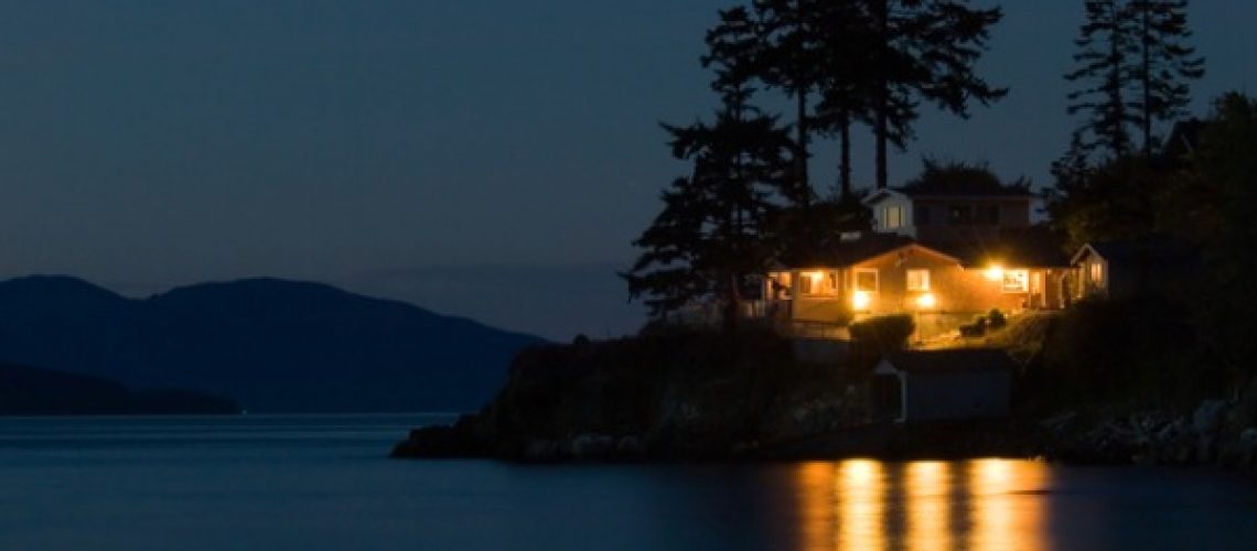 A home on the lake with all of the lights on, powered by whole home back up Generac generator by Generator Supercenter.